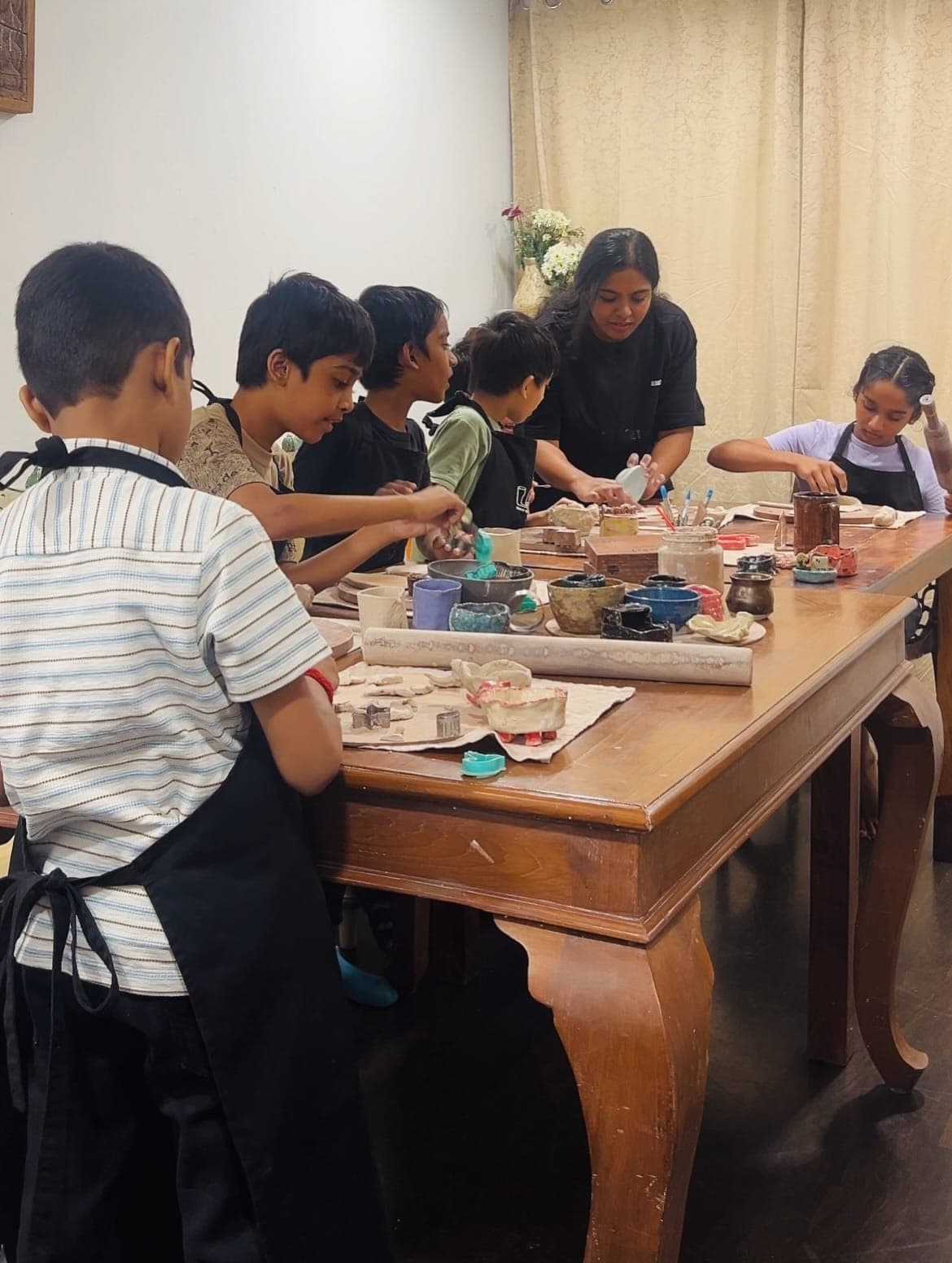 A class working with clay around the studio table, a tutor helping