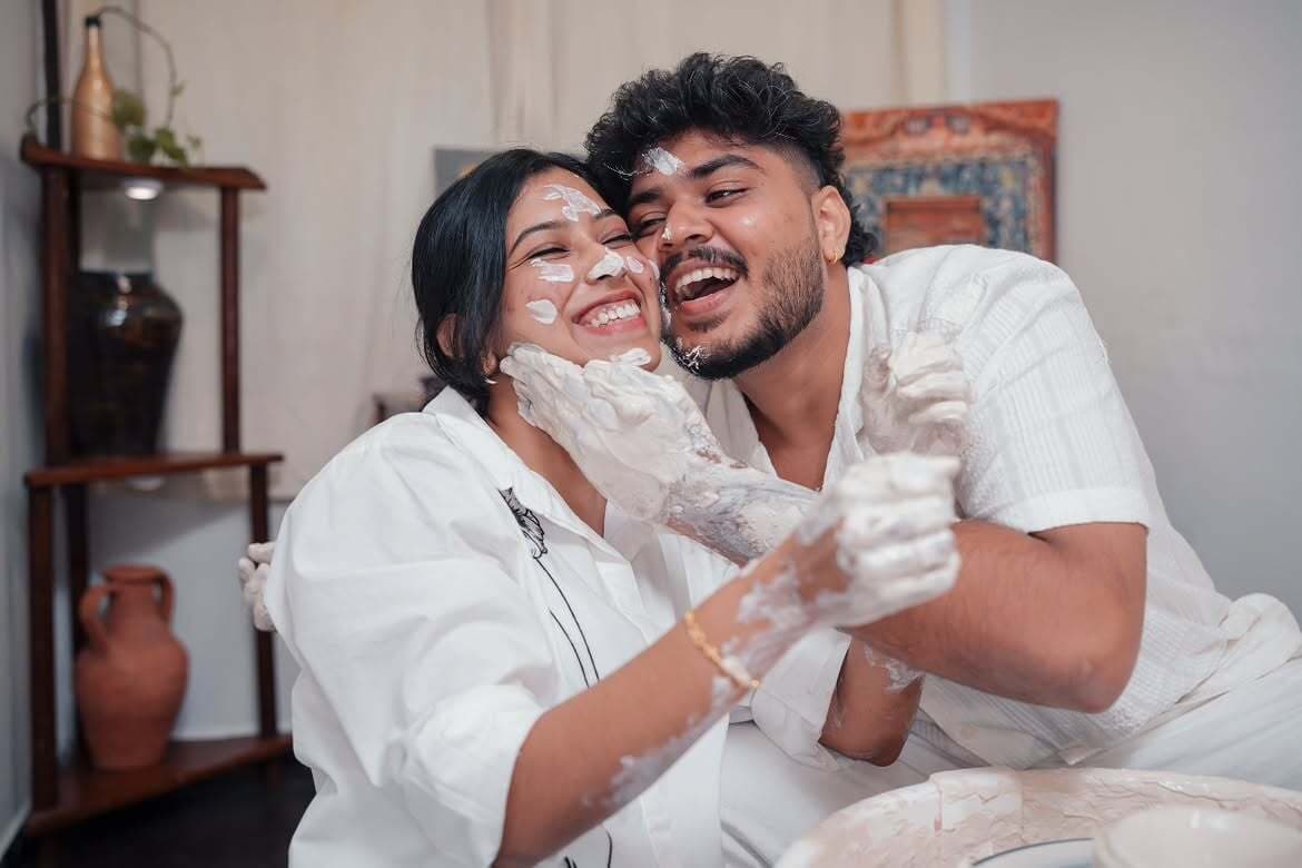 A couple laughing with wet clay on their hands and faces at the studio